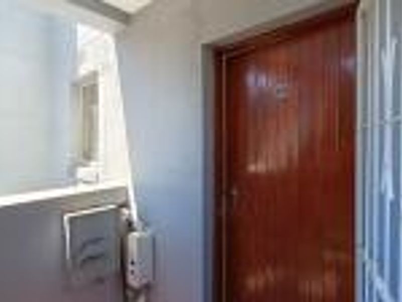 A secure apartment entrance featuring a solid wood door and a protective security gate in a well-maintained exterior corridor.