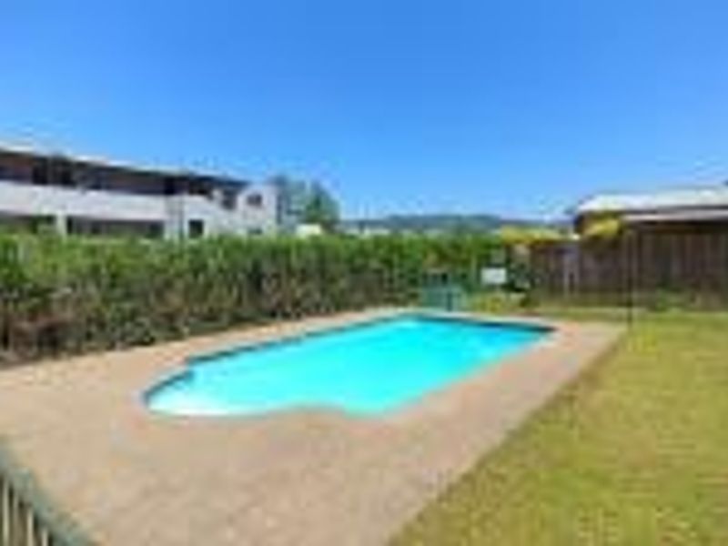 Outdoor swimming pool area featuring a paved surround, perimeter fencing, and established garden hedging within a residential apartment complex.