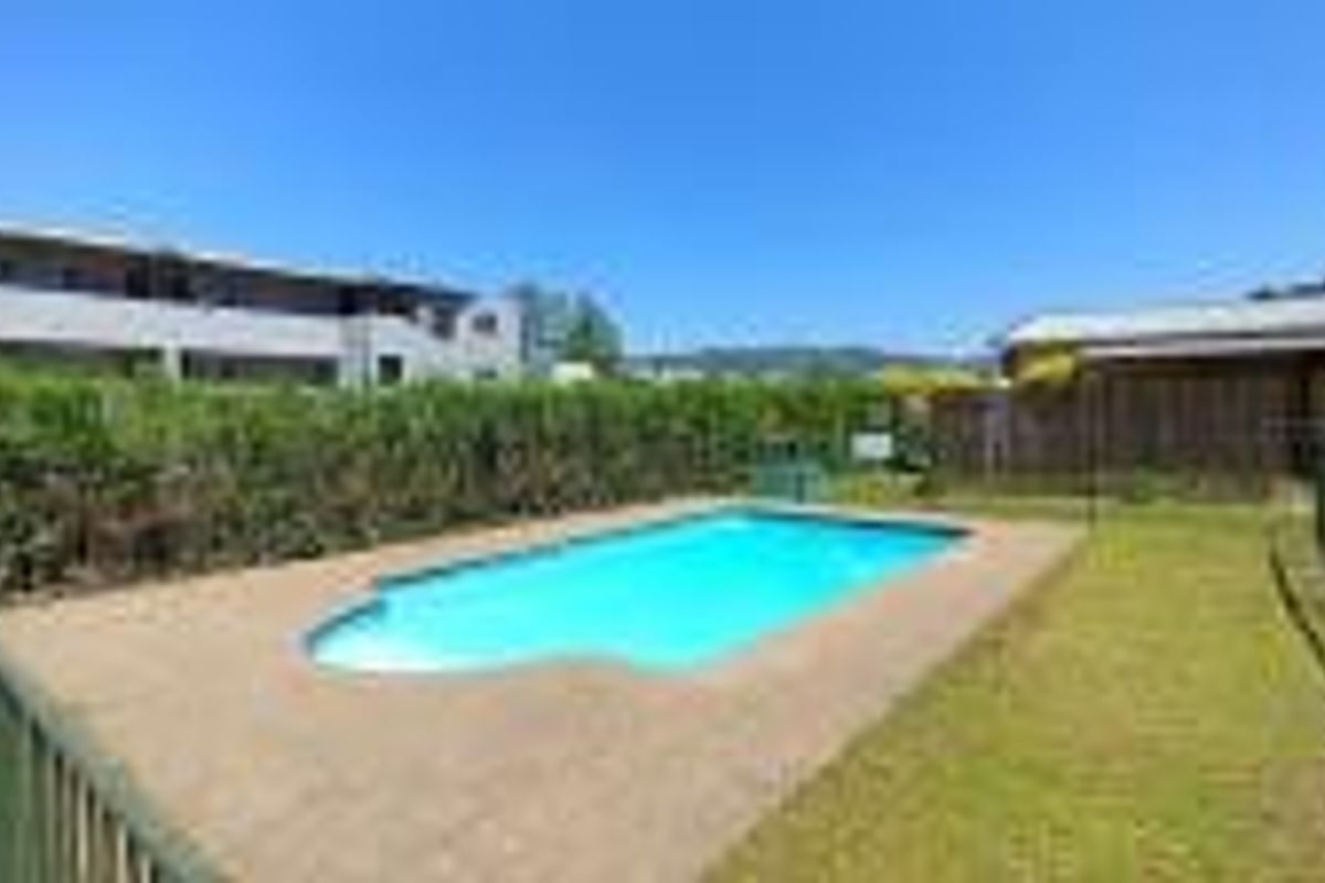 Outdoor swimming pool area featuring a paved surround, perimeter fencing, and established garden hedging within a residential apartment complex.