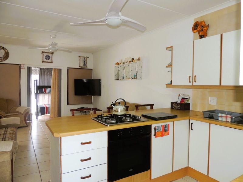 Open-plan kitchen and living area featuring built-in cabinetry, gas hob, oven, and tiled flooring, providing a functional and connected living space.