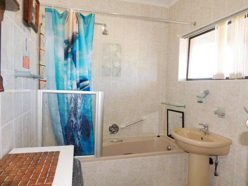 A functional bathroom featuring a pedestal basin, built-in bathtub with shower attachment, and neutral wall tiling.