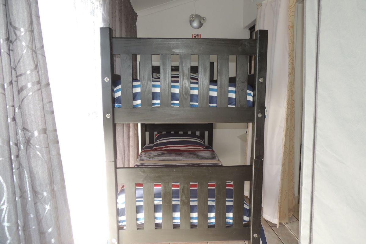 A compact bedroom featuring tiled flooring and a wall-mounted light fixture, currently furnished with a bunk bed.