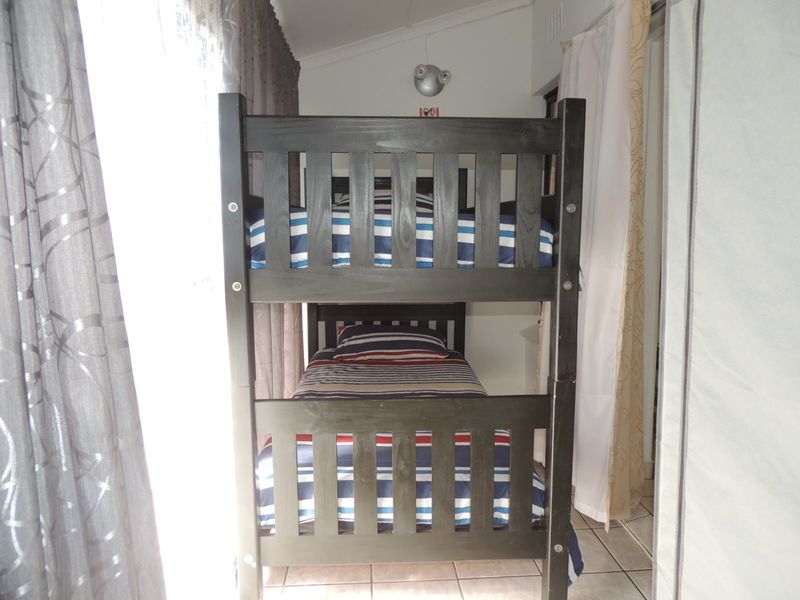 A compact bedroom featuring tiled flooring and a wall-mounted light fixture, currently furnished with a bunk bed.