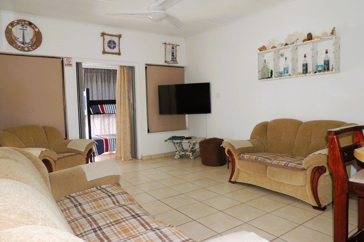 A living room featuring tiled flooring, a ceiling fan, and access to an adjacent bedroom area through a sliding door.