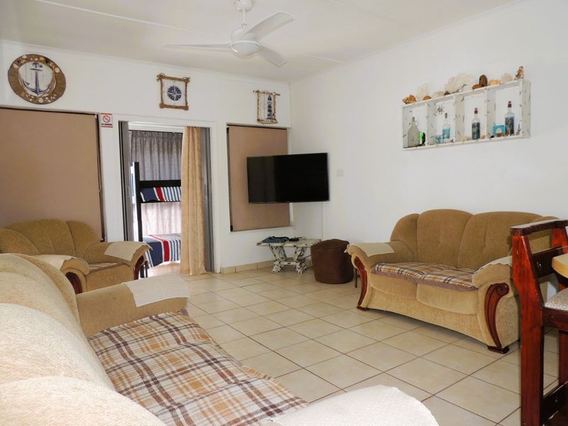 A living room featuring tiled flooring, a ceiling fan, and access to an adjacent bedroom area through a sliding door.