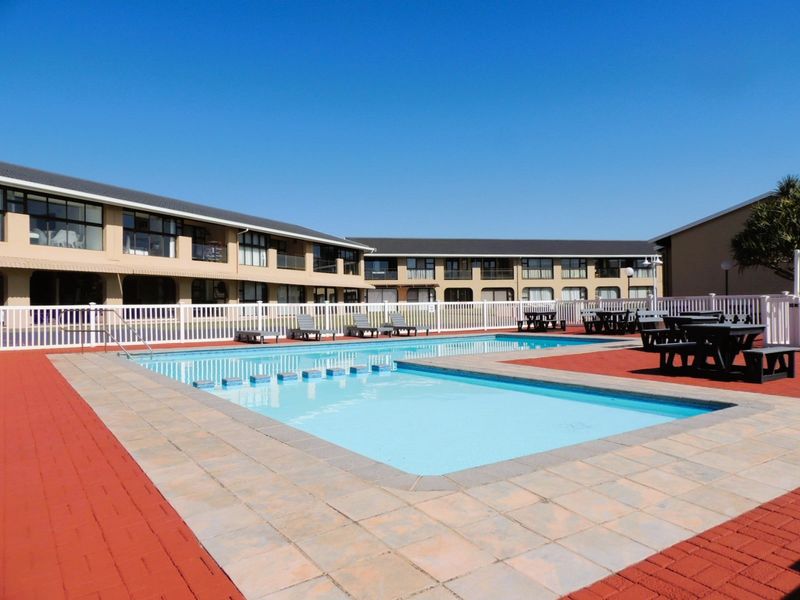 A well-maintained communal swimming pool area surrounded by paved decking and a white picket fence, set against a multi-story apartment complex.