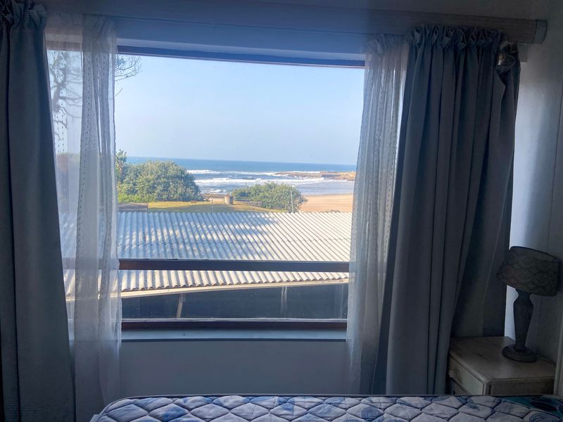 A bedroom window offering a scenic view of the coastline, beach, and ocean.