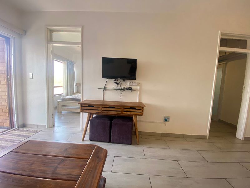 A living area featuring neutral tiled flooring and access to adjacent rooms, providing a functional and open layout.