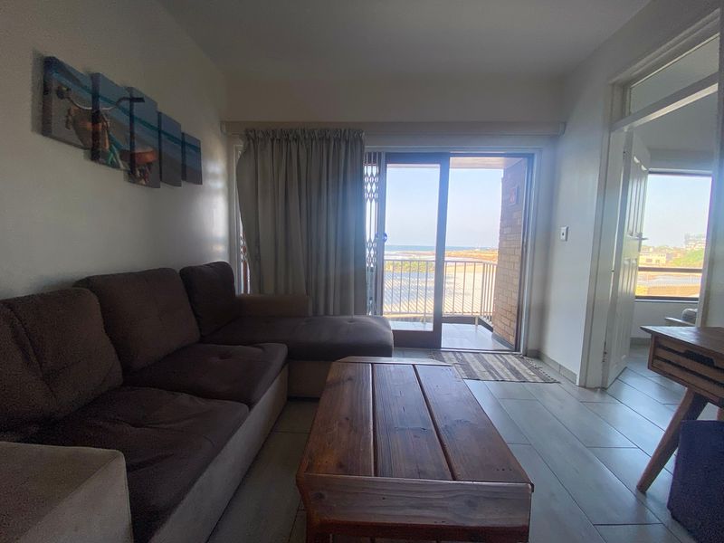 A living room featuring tiled flooring and a sliding glass door that opens onto a balcony with ocean views.