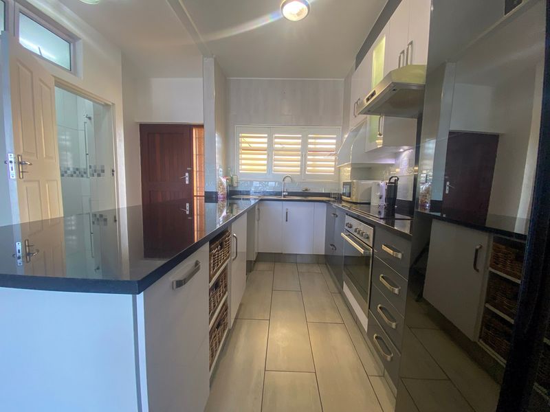 Modern kitchen featuring granite countertops, built-in oven, extractor fan, and ample cabinetry, with tiled flooring and a functional layout.