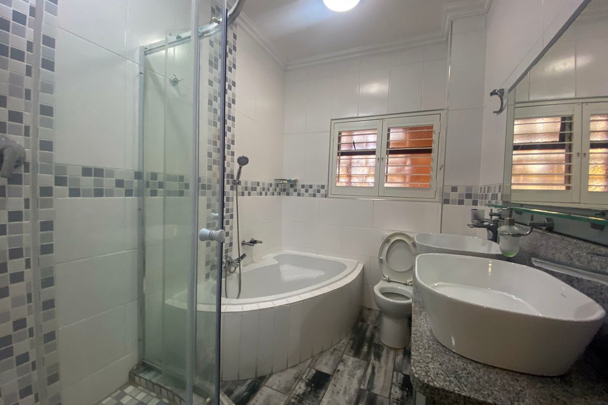 A well-appointed bathroom featuring a corner bathtub, glass shower enclosure, dual vessel sinks on a granite vanity, and tiled finishes.