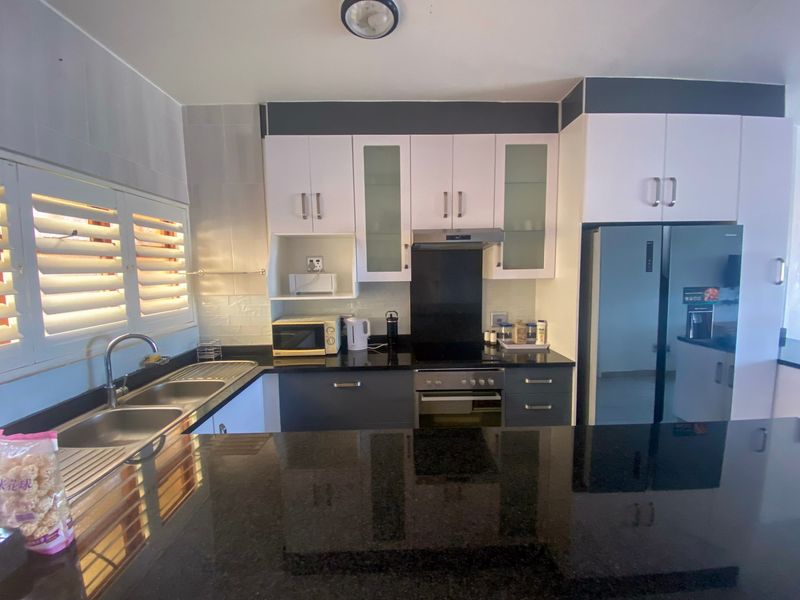 Modern kitchen featuring sleek black granite countertops, fitted white and grey cabinetry, built-in oven with extractor fan, and double sink with shutter blinds.