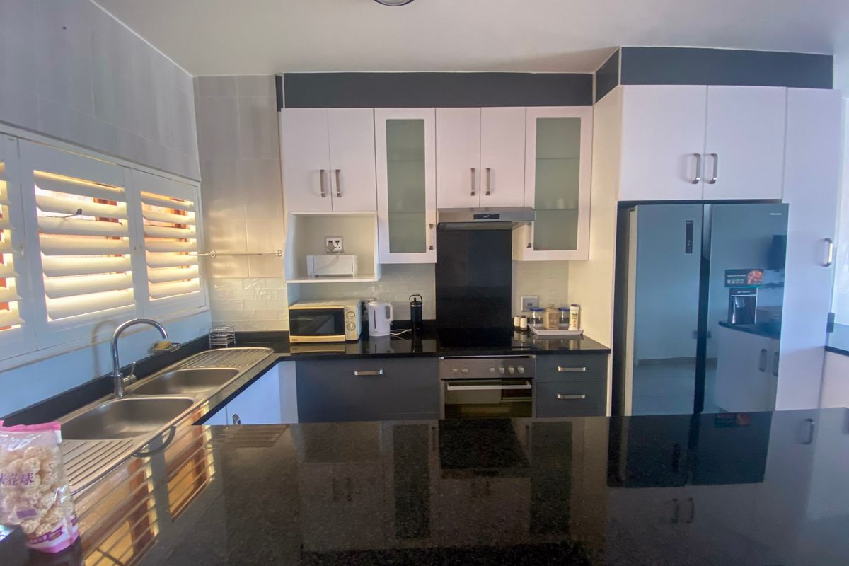 Modern kitchen featuring sleek black granite countertops, fitted white and grey cabinetry, built-in oven with extractor fan, and double sink with shutter blinds.