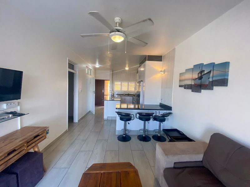 Open-plan living and kitchen area featuring tiled flooring, a breakfast bar with granite countertops, and a ceiling fan.