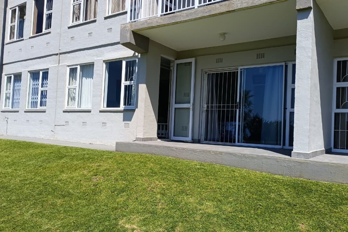 Rear view of the apartment building featuring a concrete patio, sliding glass doors with security gates, and access to a communal lawn area.