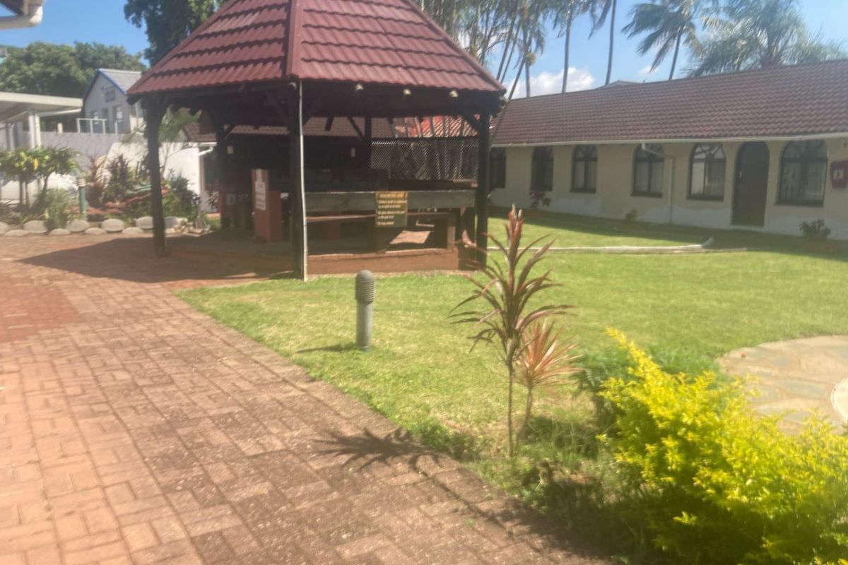 A rear garden area featuring a covered gazebo, paved pathways, and a well-maintained lawn adjacent to the apartment building.