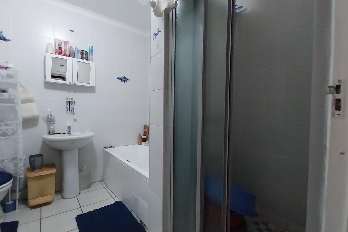 A functional bathroom featuring a pedestal basin, a built-in bathtub, and a separate shower enclosure with tiled finishes throughout.