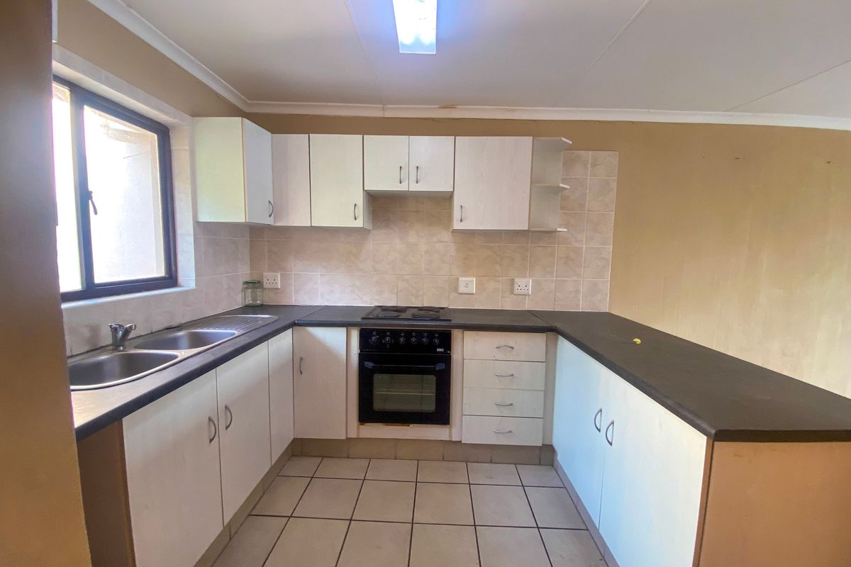 A functional kitchen featuring white cabinetry, dark laminate countertops, a built-in oven and hob, and tiled flooring, offering a clean, blank canvas for updates.