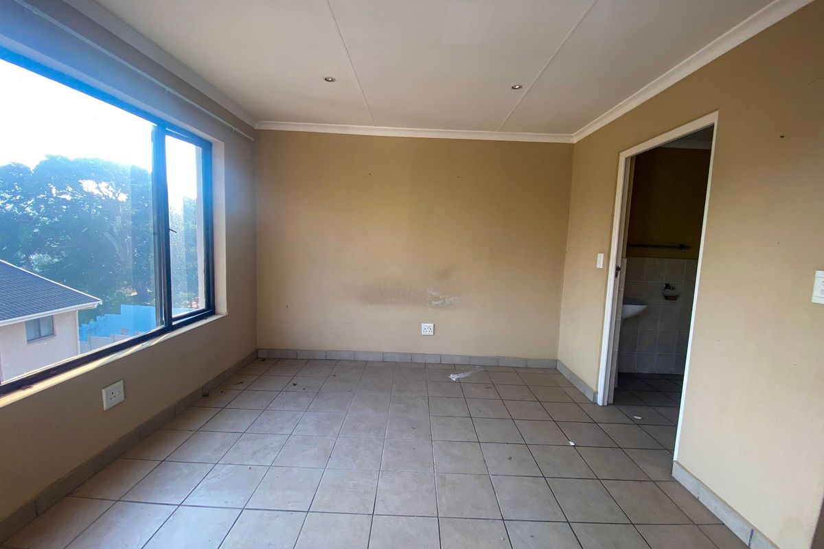 An empty bedroom featuring tiled flooring, recessed downlights, and an adjoining bathroom, offering a blank canvas for personalization.