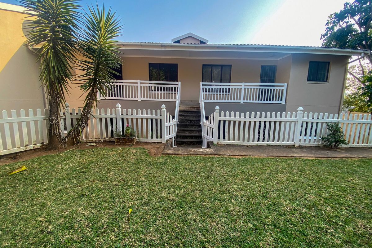 Rear view of the apartment featuring a raised balcony, white picket fencing, and concrete stairs leading to the garden area.
