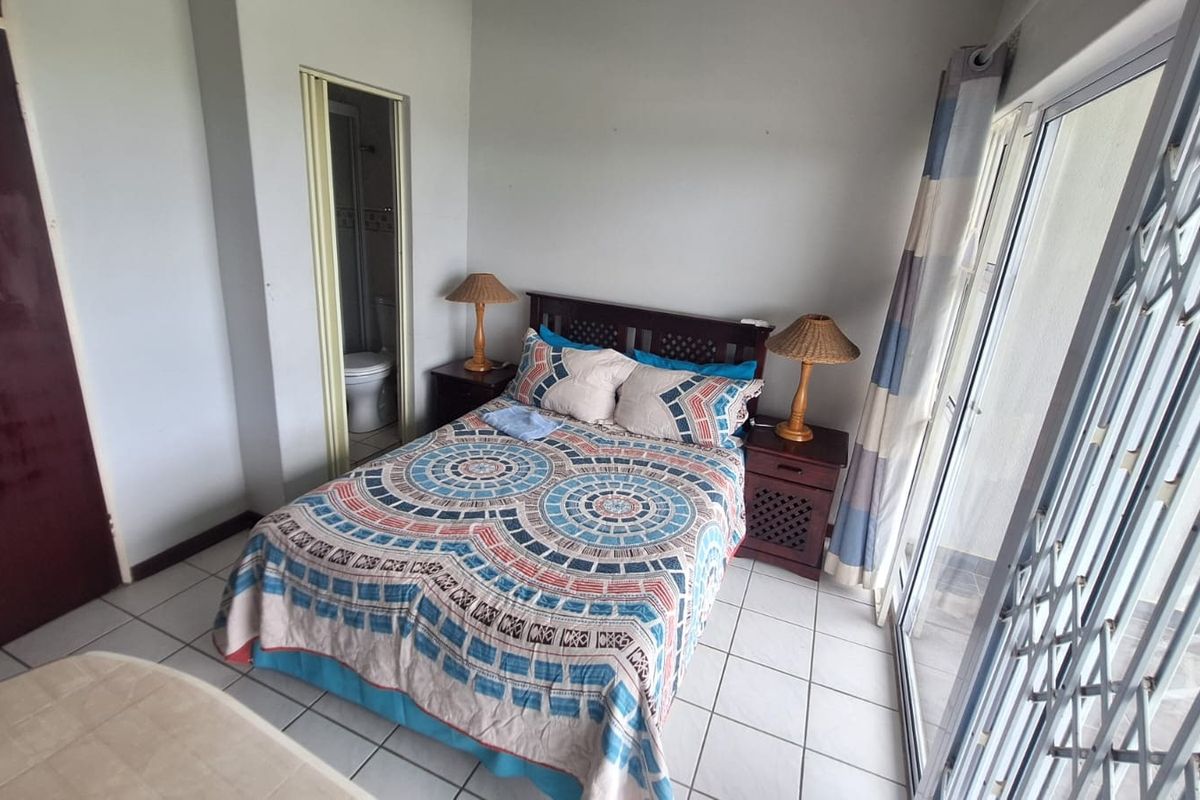 A bedroom featuring tiled flooring, a built-in cupboard, and an en-suite bathroom, with direct access to an outdoor area through a sliding glass door.