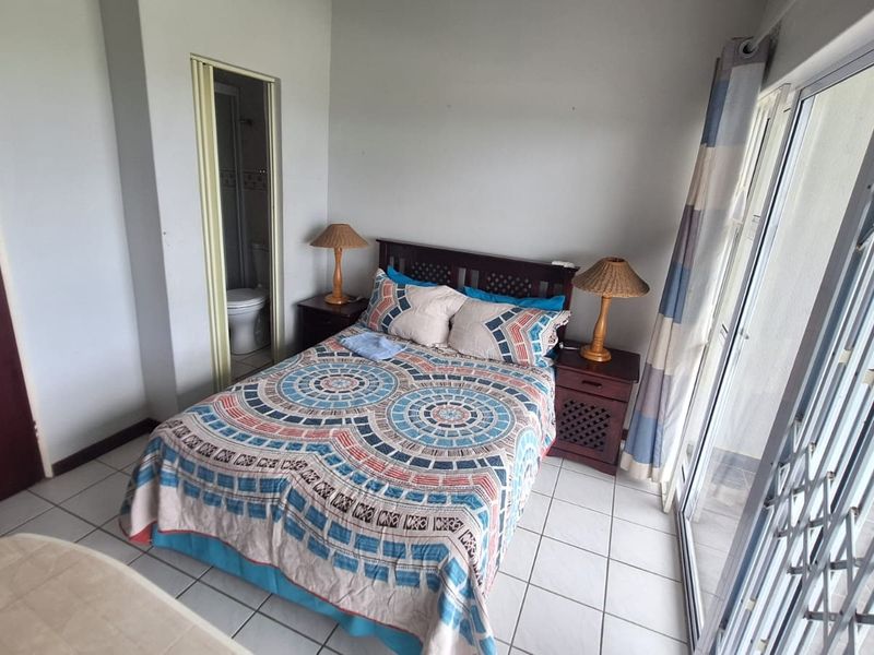 A bedroom featuring tiled flooring, a built-in cupboard, and an en-suite bathroom, with direct access to an outdoor area through a sliding glass door.