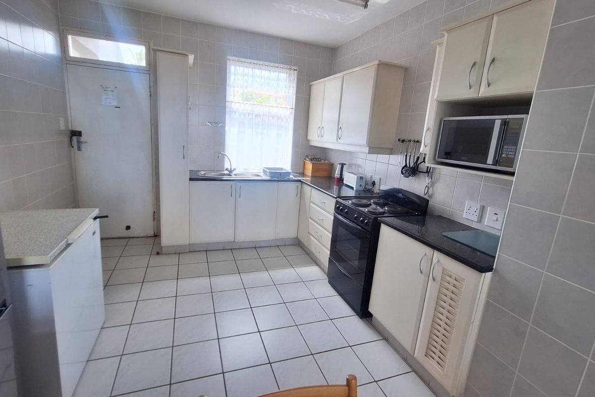A functional kitchen featuring tiled walls and floors, ample built-in cabinetry, laminate countertops, and a built-in microwave with a freestanding stove.