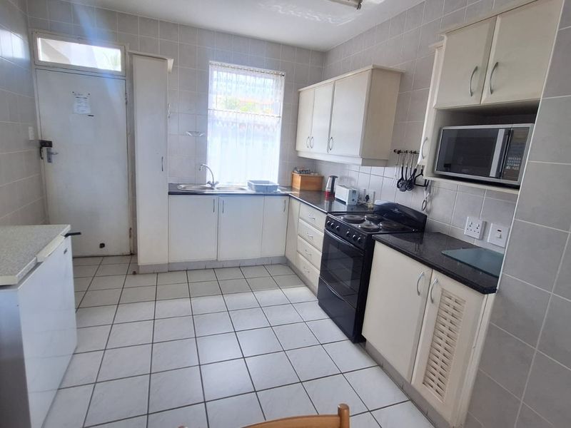 A functional kitchen featuring tiled walls and floors, ample built-in cabinetry, laminate countertops, and a built-in microwave with a freestanding stove.