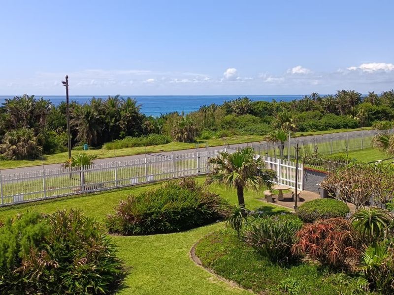 Elevated view overlooking a well-maintained garden, perimeter fencing, and coastal landscape with ocean horizon in the distance.