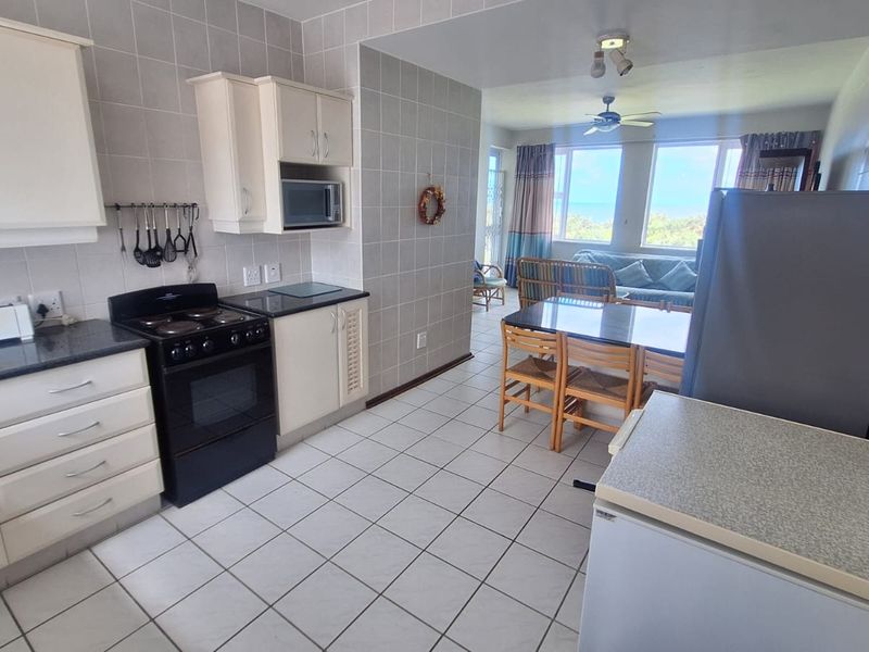 Open-plan kitchen and living area featuring tiled finishes, built-in cabinetry, and an electric stove, with direct access to a bright living space.
