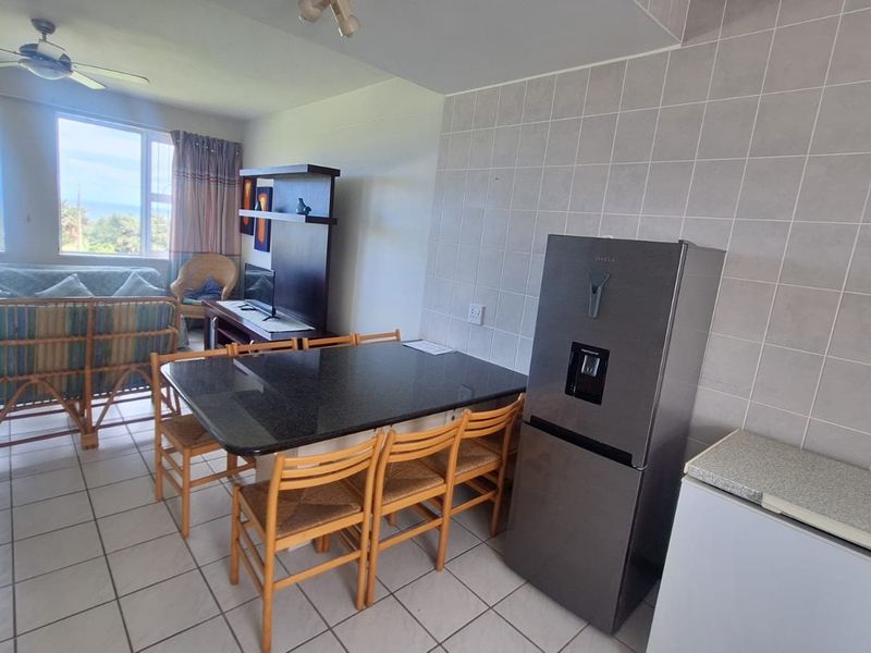 Open-plan living and dining area featuring tiled flooring, a ceiling fan, and a functional kitchen space with tiled splashbacks.