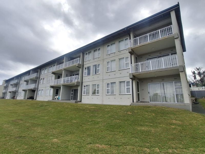 A multi-story apartment building exterior featuring private balconies with metal railings, sliding glass doors, and a well-maintained lawn area.