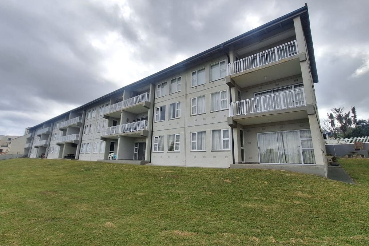 A multi-story apartment building exterior featuring private balconies with metal railings, sliding glass doors, and a well-maintained lawn area.