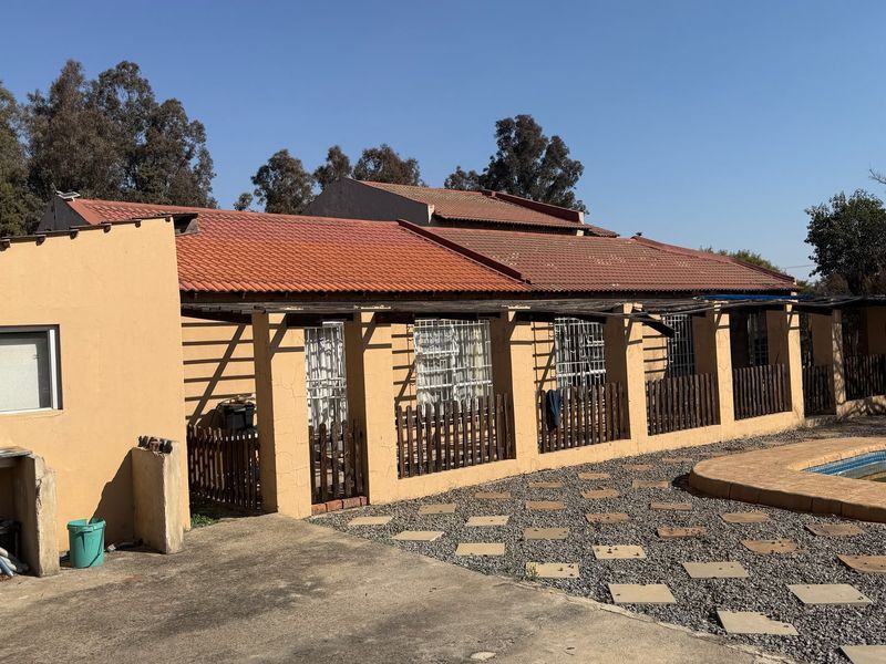 Rear view of the house featuring a tiled roof, covered patio area with timber fencing, and an adjacent swimming pool in a paved garden setting.