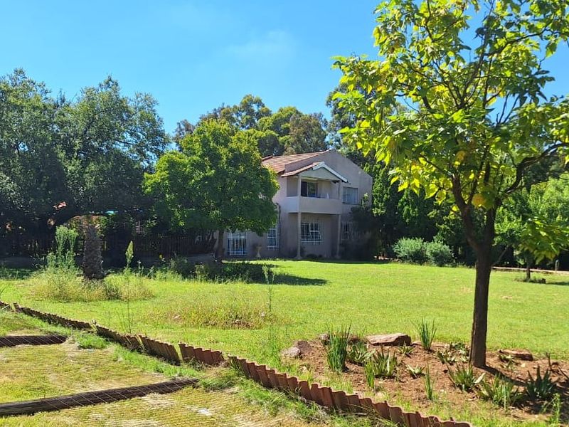 A view of the rear elevation of a two-story house set within a large, established garden with mature trees and lawn.