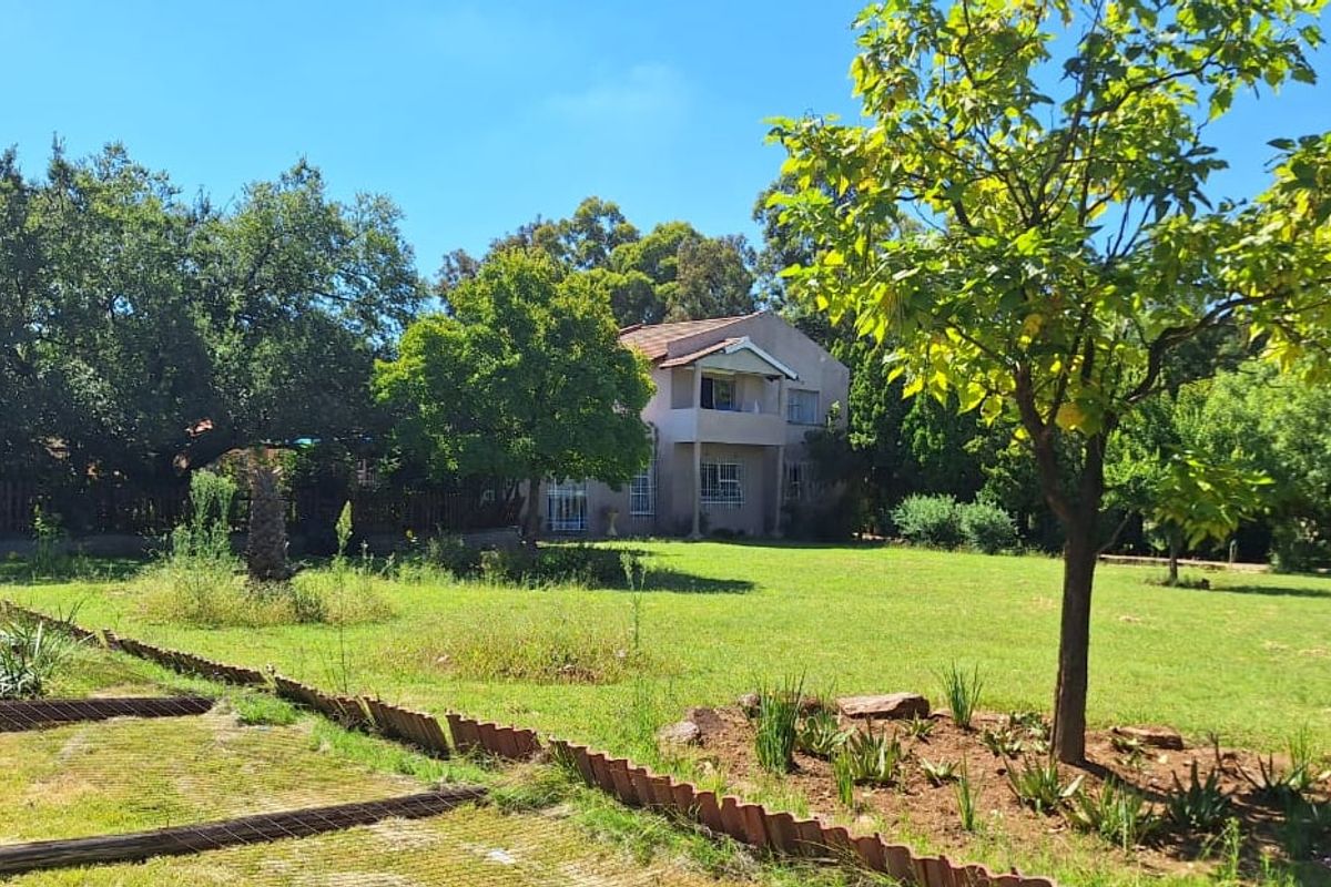 A view of the rear elevation of a two-story house set within a large, established garden with mature trees and lawn.