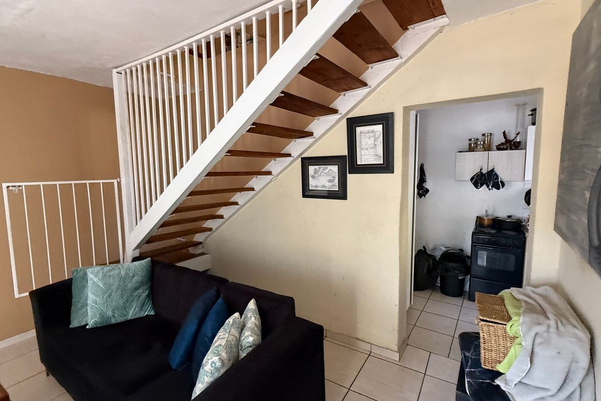 Living area featuring an open staircase with white balustrades, leading to a compact kitchen area with tiled flooring.