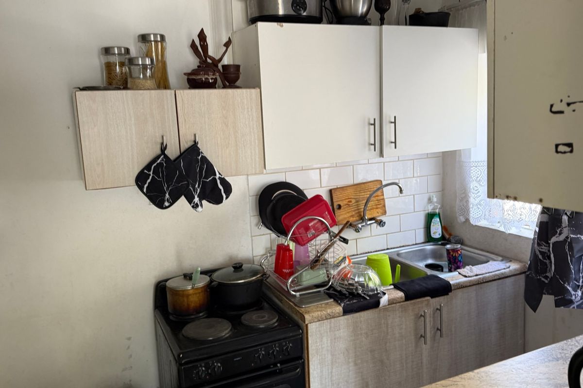 Compact kitchen area featuring built-in cabinetry, a stainless steel sink, and a freestanding electric stove with tiled splashback.