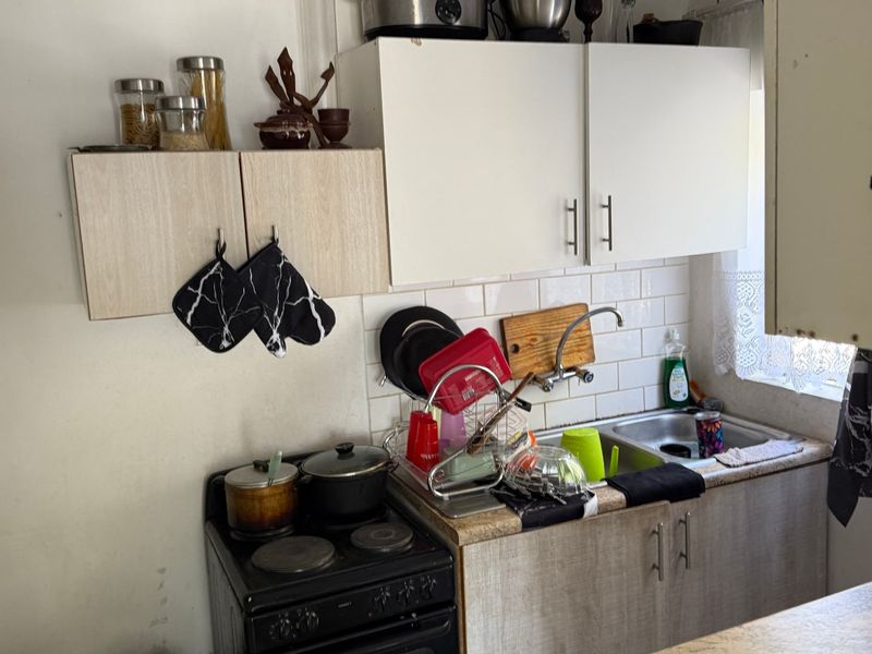 Compact kitchen area featuring built-in cabinetry, a stainless steel sink, and a freestanding electric stove with tiled splashback.