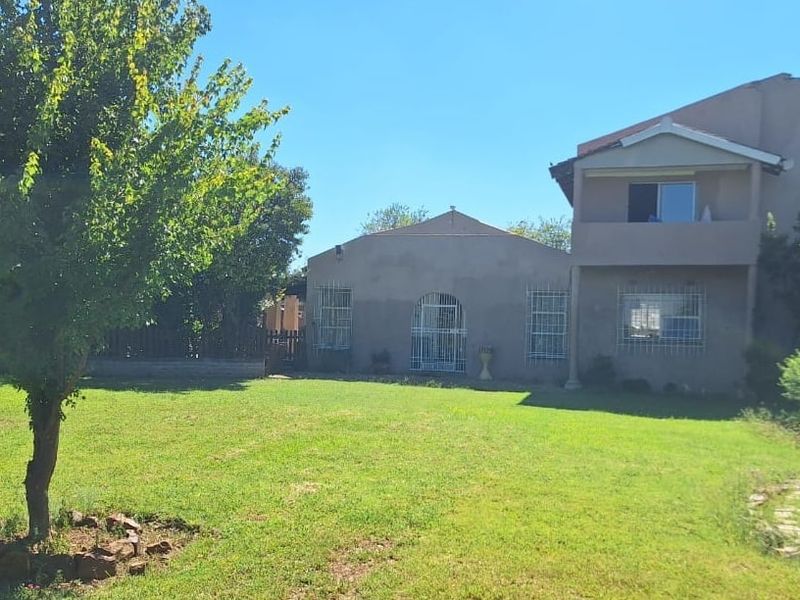 A view of the rear exterior of the house, featuring a large garden area and a multi-level building structure with security bars on windows.