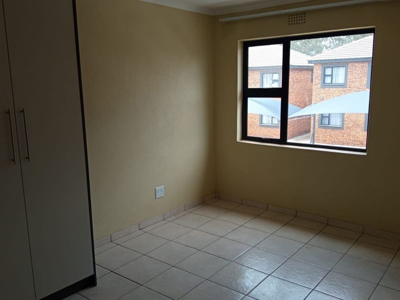 A clean, empty bedroom featuring tiled flooring, a built-in wardrobe, and a large window providing natural light.