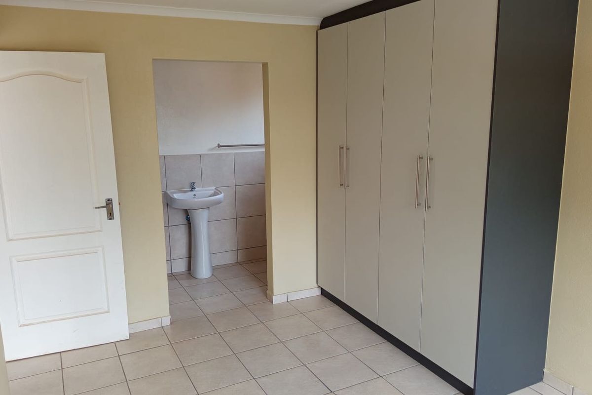 A clean, empty bedroom featuring built-in wardrobes and an en-suite bathroom with a pedestal basin and tiled finishes.
