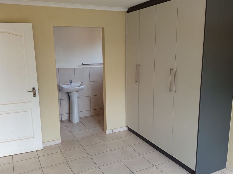 A clean, empty bedroom featuring built-in wardrobes and an en-suite bathroom with a pedestal basin and tiled finishes.