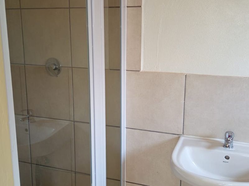 A functional bathroom featuring a glass shower enclosure, pedestal basin, and neutral ceramic tiling throughout.