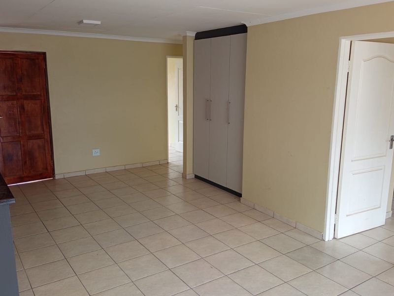 An open-plan living area featuring tiled flooring, built-in cupboards, and direct access to adjacent rooms and kitchen space.