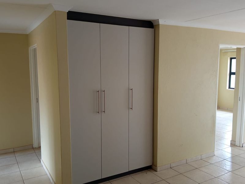 A clean, empty hallway featuring neutral tiled flooring and modern built-in cupboards with sleek handles, providing ample storage space.
