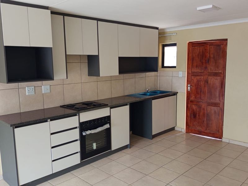 A clean, modern kitchen featuring two-tone cabinetry, granite countertops, a built-in oven and hob, and neutral tiled flooring.