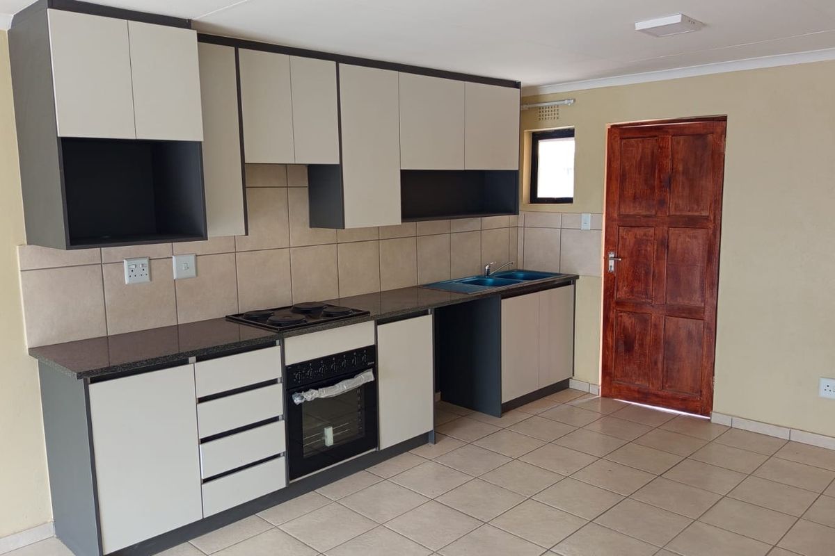 A clean, modern kitchen featuring two-tone cabinetry, granite countertops, a built-in oven and hob, and neutral tiled flooring.