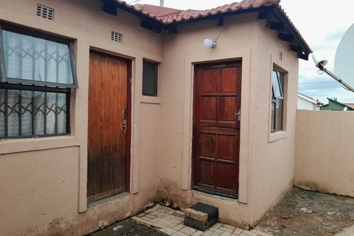 Rear exterior view of the property featuring plastered walls, timber doors, security bars on windows, and a paved outdoor area.