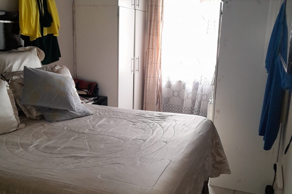 A bedroom featuring built-in cupboards, tiled flooring, and a window with natural light. The space requires cosmetic updates to improve its overall finish.